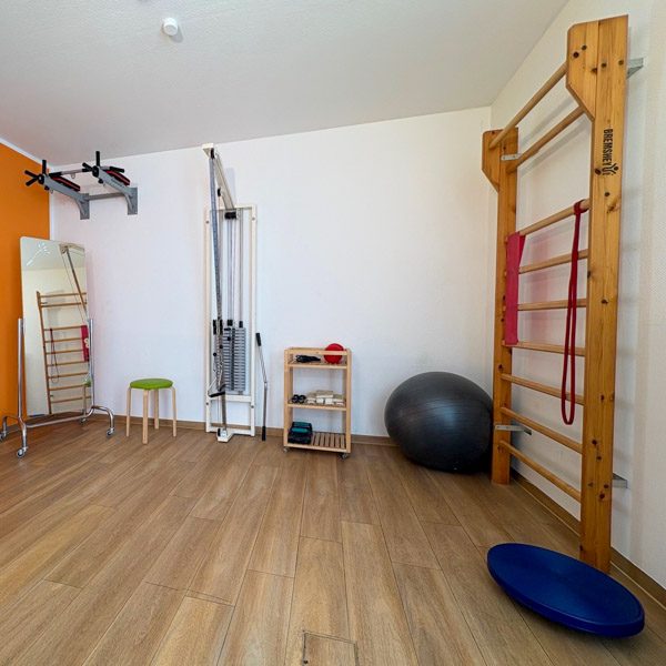 Raum mit Trainingsgeräten: Sprossenwand, Gymnastikball, Hanteln und Matte.