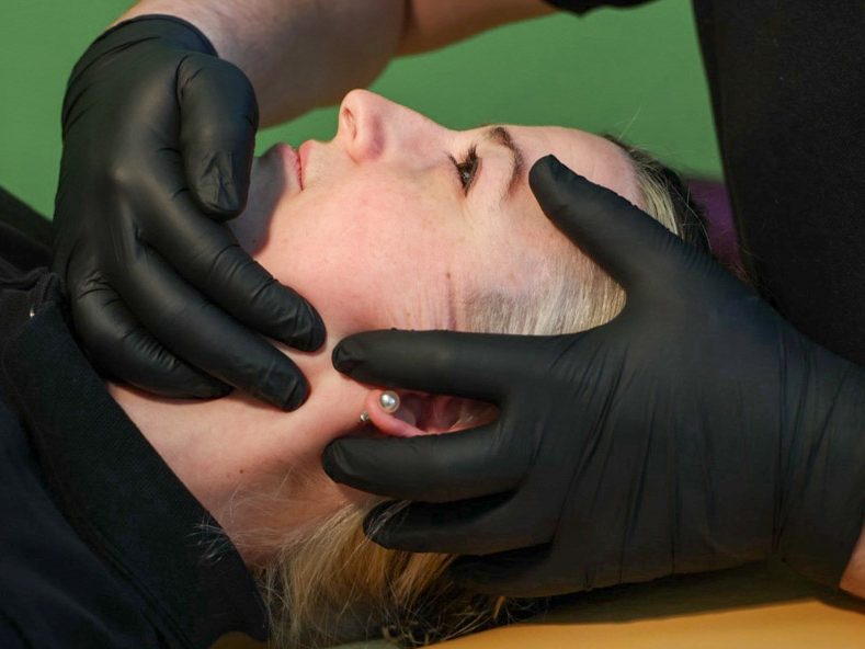 Eine Person erhält eine Gesichtsbehandlung, Hände mit schwarzen Handschuhen berühren das Gesicht.